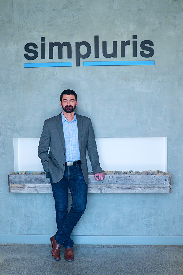 Jacob Kamenir stands in front of the Simpluris company logo